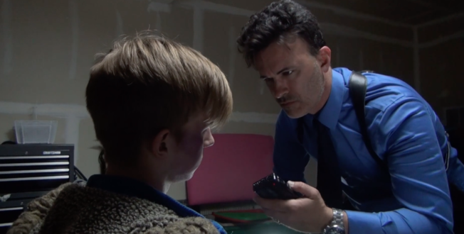 Screenshot from "The Collective" A man is holding a recorder up to a teenager that he has tied to a chair. 